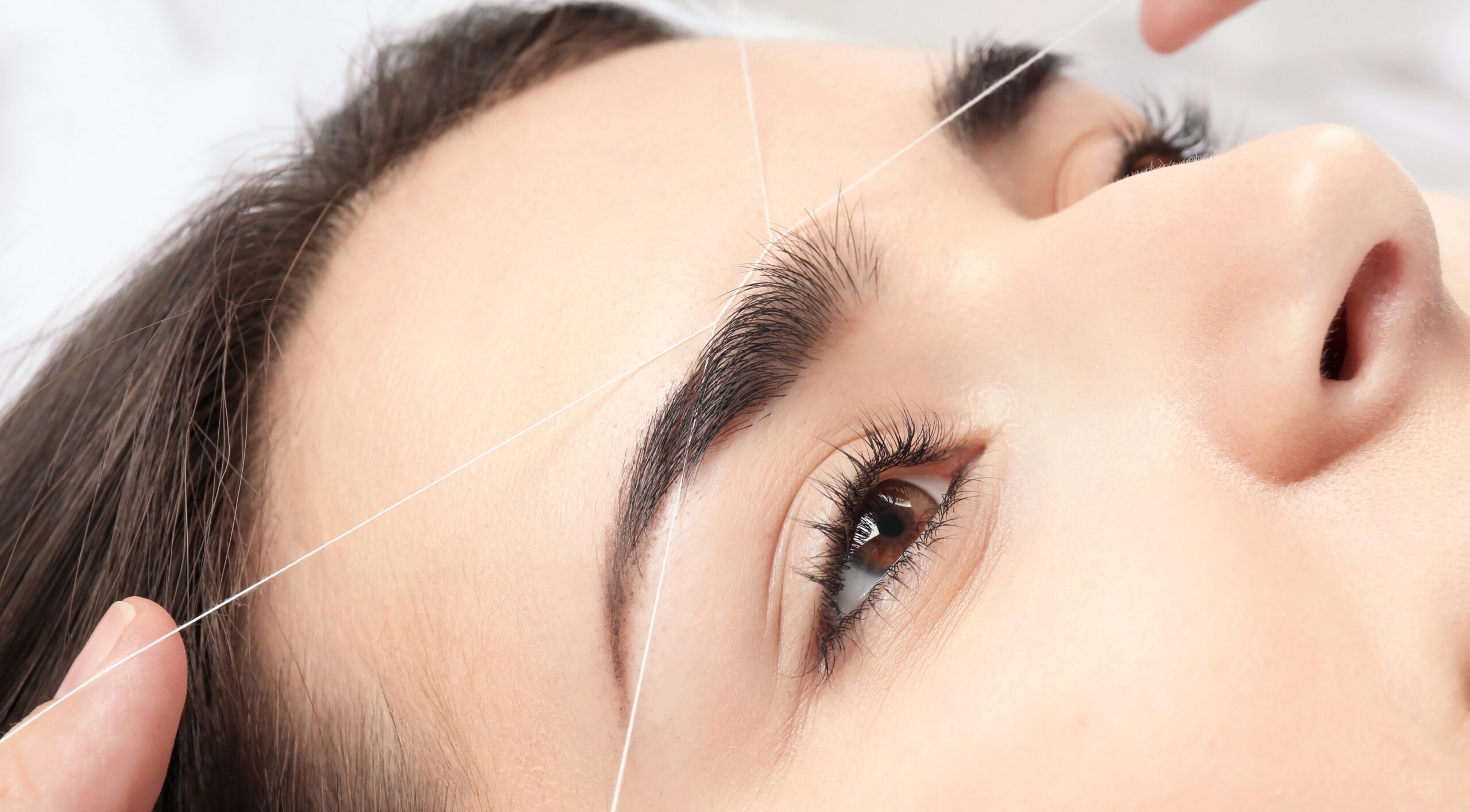 Young woman having professional eyebrow correction procedure in beauty salon, closeup